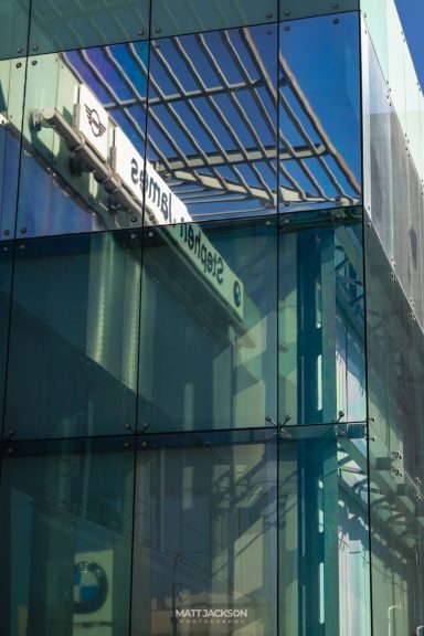 Building facade with glass panels reflecting a blue sky and structural elements.