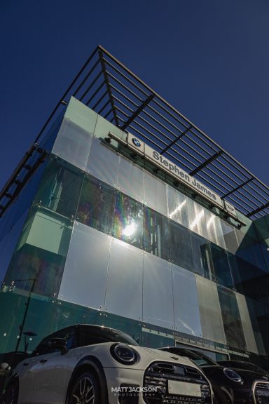 Modern glass-fronted building with a car parked in front under a clear blue sky.